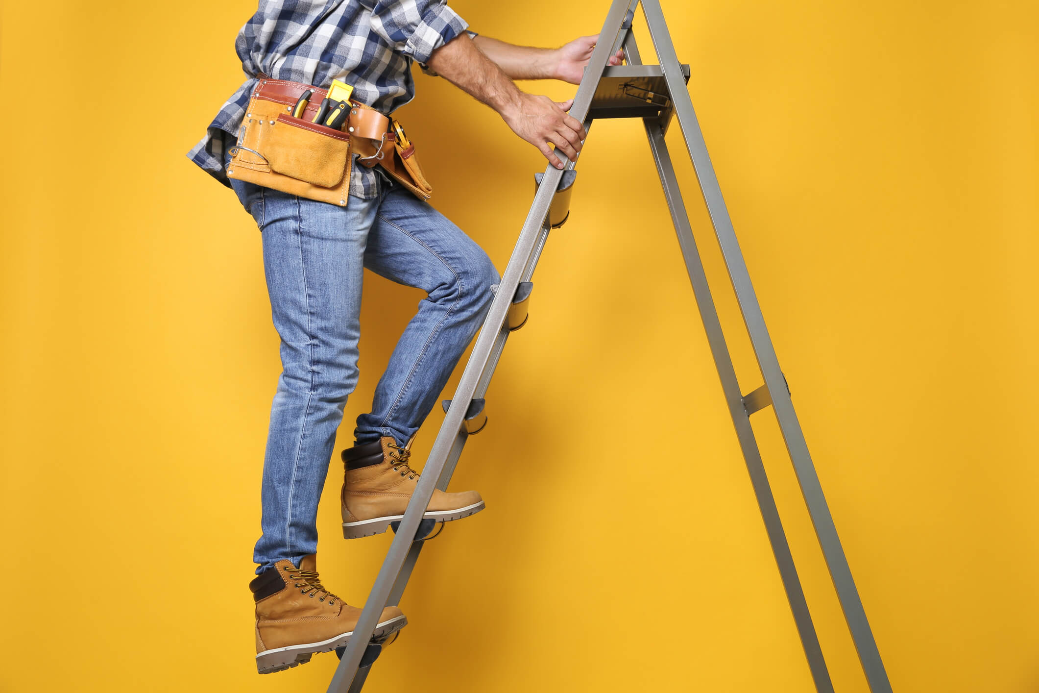 Professional builder climbing up metal ladder on yellow background, closeup