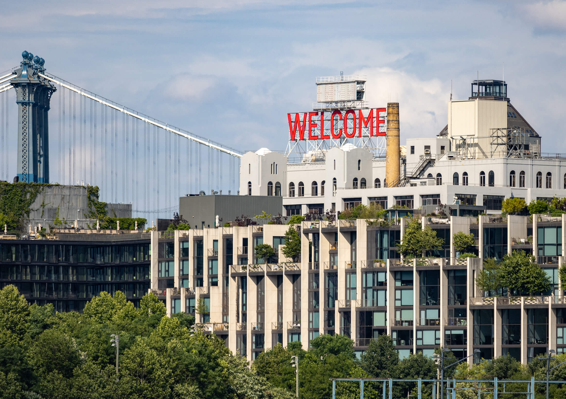 a waterfront view of the welcome sign and the manhattan bridge