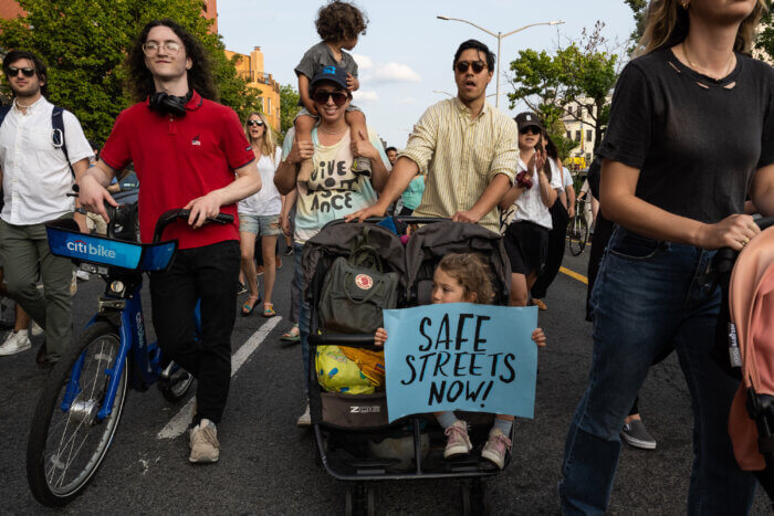 a child in a stroller holding a sign reading safe streets now!