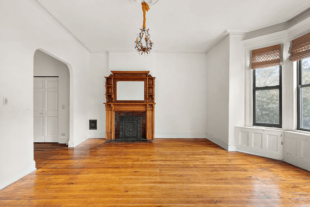 street facing room with wood mantel, moldings and an arched opening to middle room