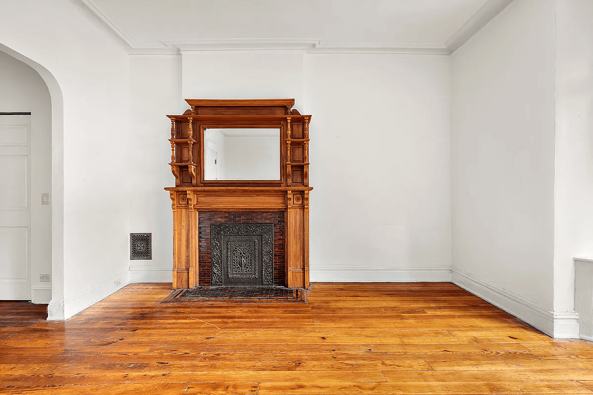 street facing room with wood mantel, moldings and an arched opening to middle room