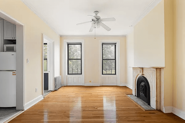 a living room with a mantel and a glimpse of the adjoining kitchen