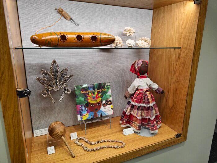 a glass case with an exhibit of objects including a neckace a doll  and a book