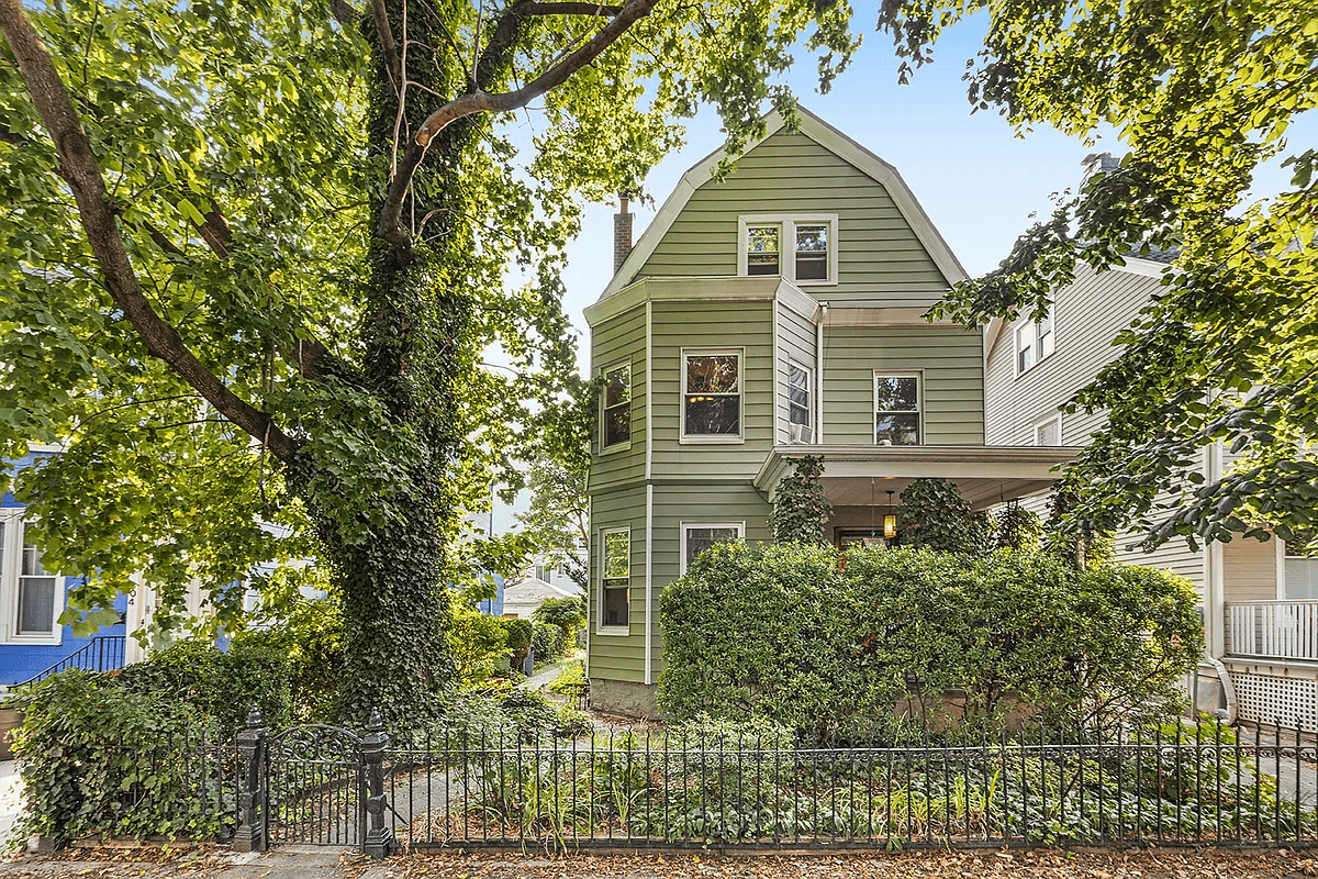 view of the green sided house with greenery covered front porch