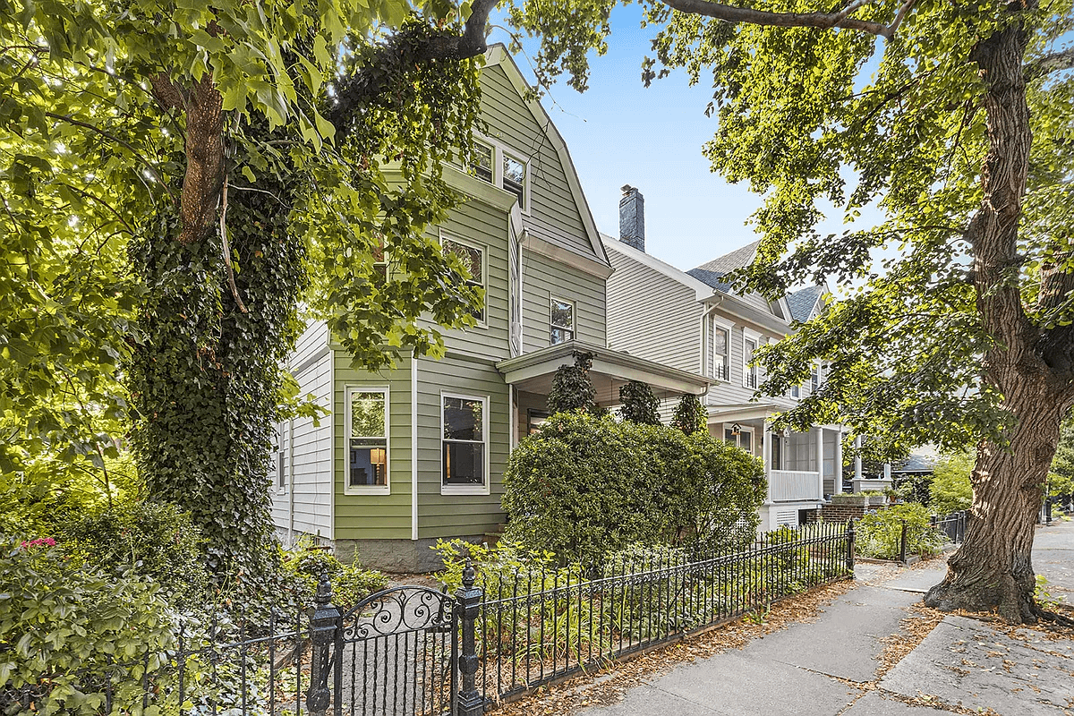 view of the green sided house with greenery covered front porch