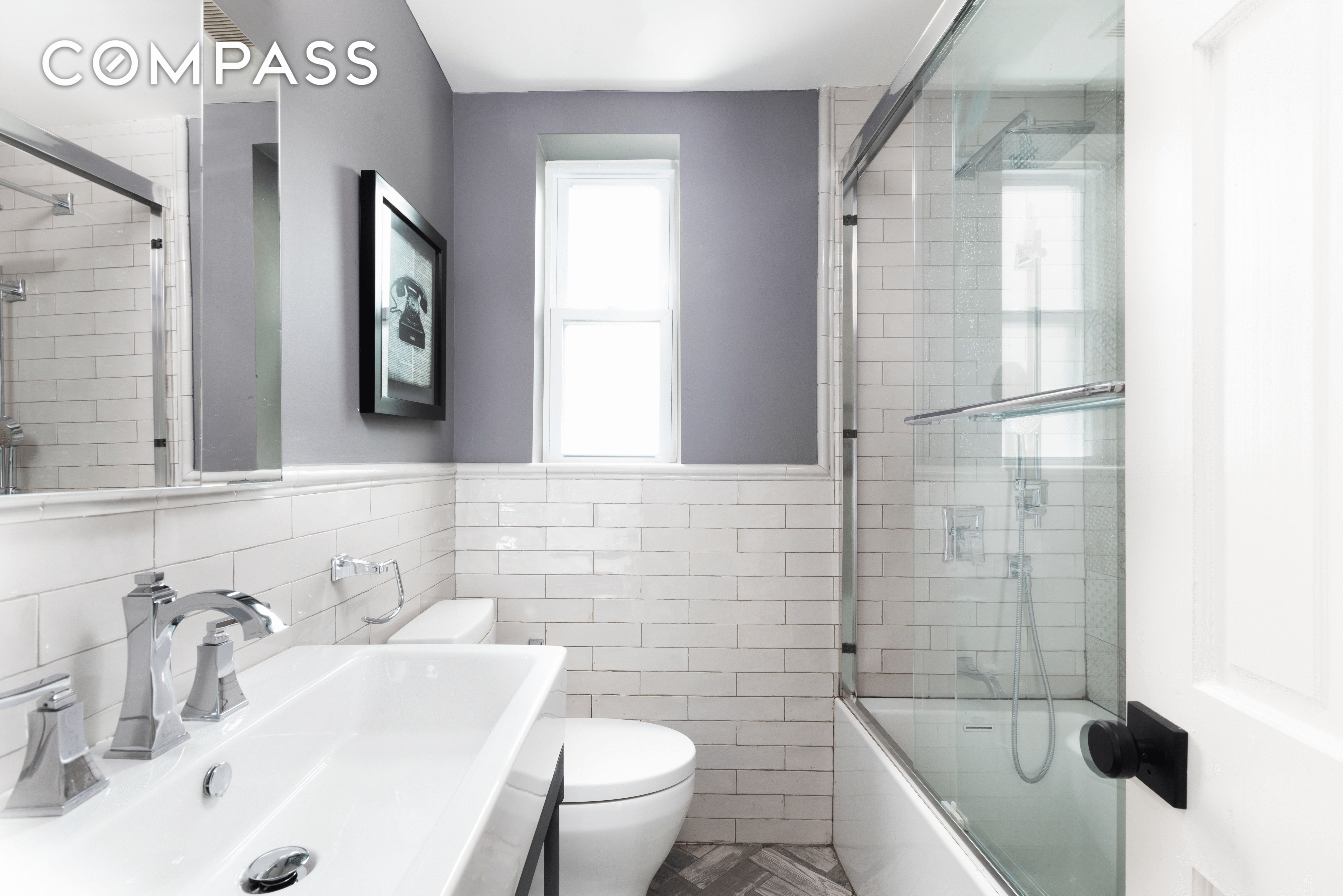 a bathroom with white fixtures, glass shower doors and white subway tile walls