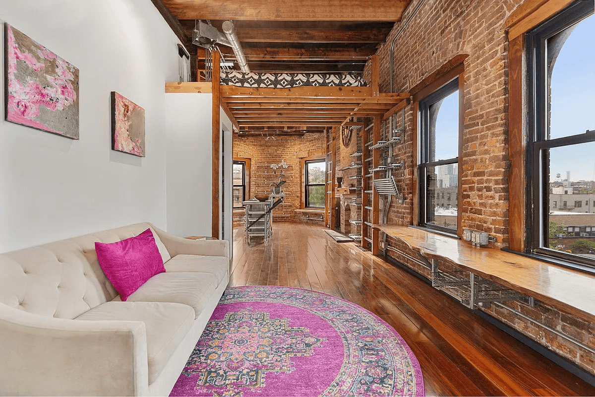 view from living room to kitchen with lofted bed and exposed brick wall