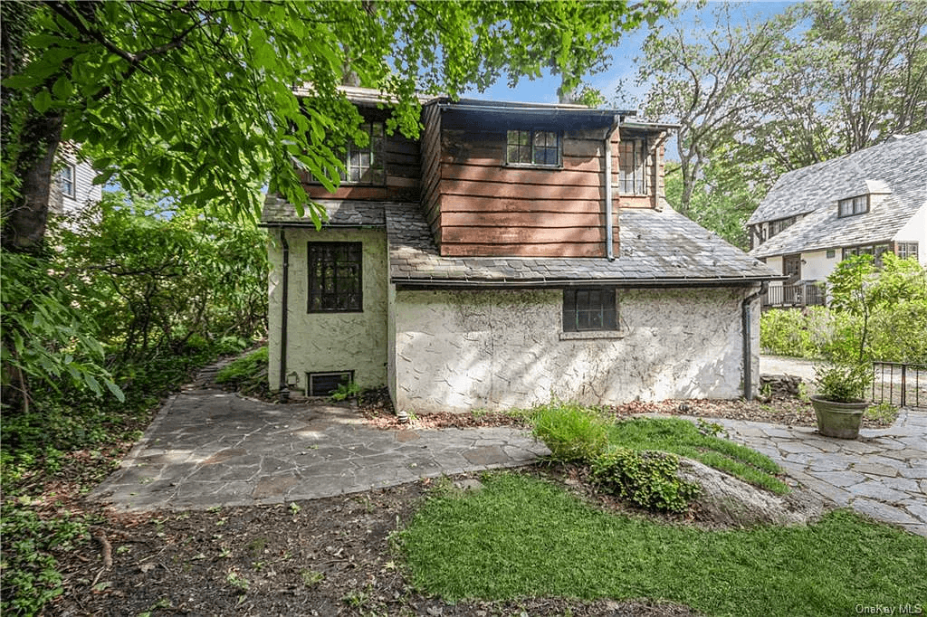 rear facade with stucco lower floor and wood sided upper level and with a stone patio