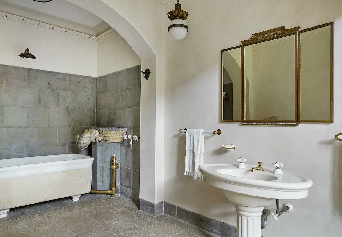 bathroom in middle duplex with gray tile, pedestal sink and nook for the soaking tub