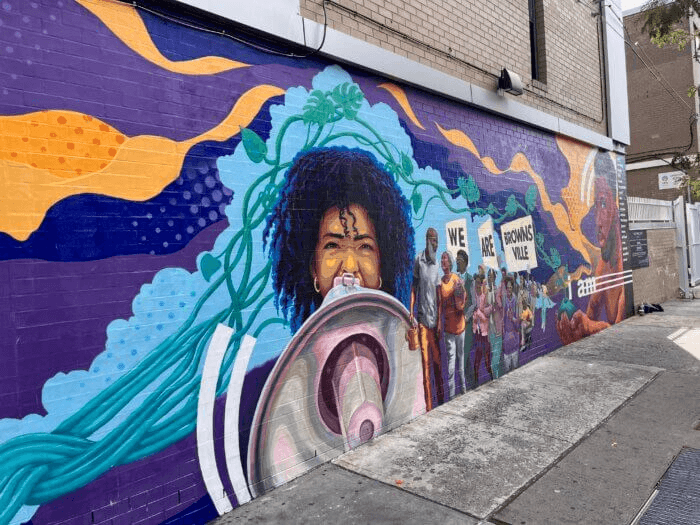 mural in bright colors depicts a person with a megaphone and people holding signs