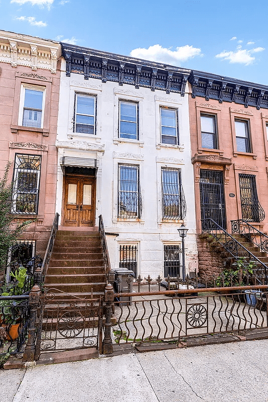 exterior of white painted brownstone with stoop and ironwork fence
