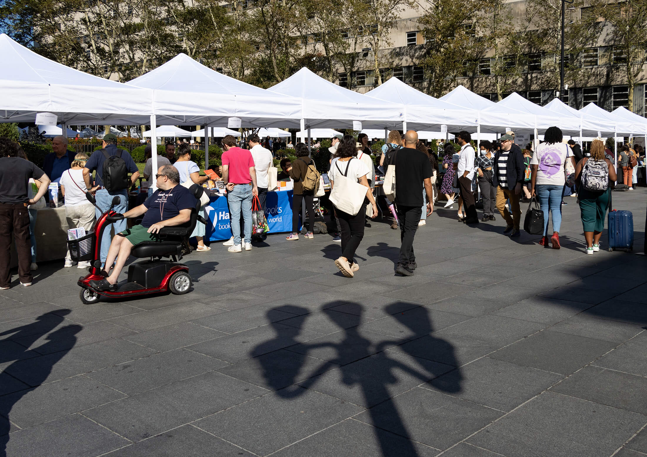 people walking by a row of book tables with white tents