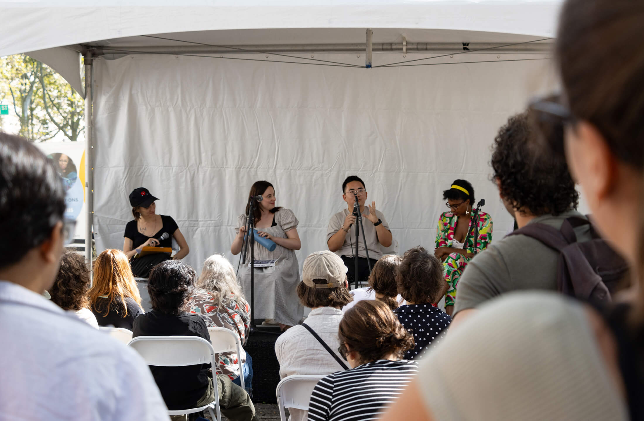 looking through a crowd to a stage with four authors speaking