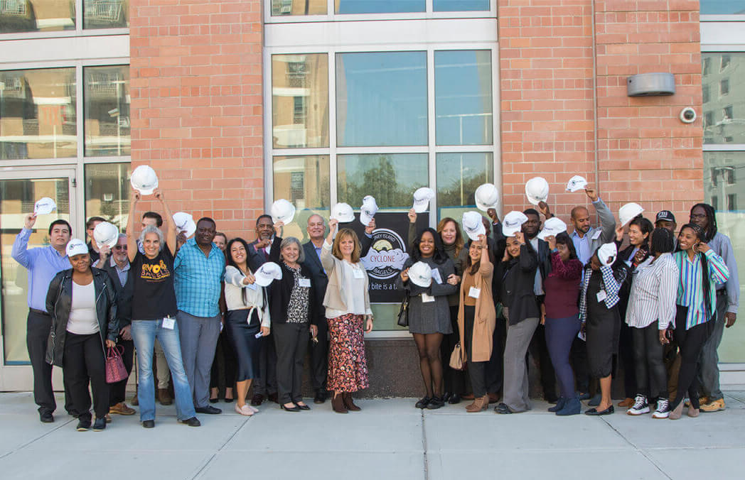 cyclone bagels - group posed outside a building with hardhats and a sign for the shop