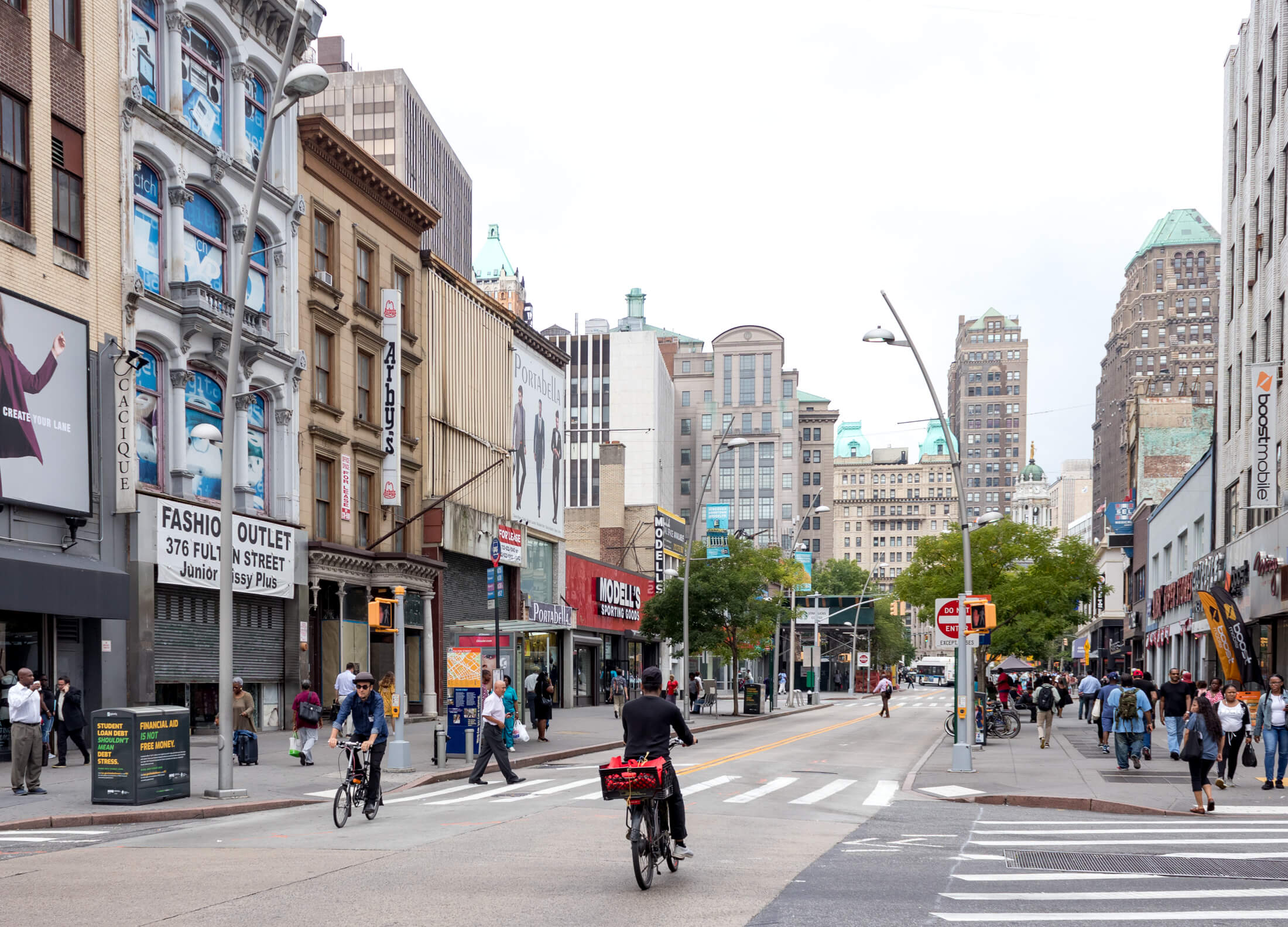 people riding bikes on Fulton Street with an Arbys sign on Gage and Tollner