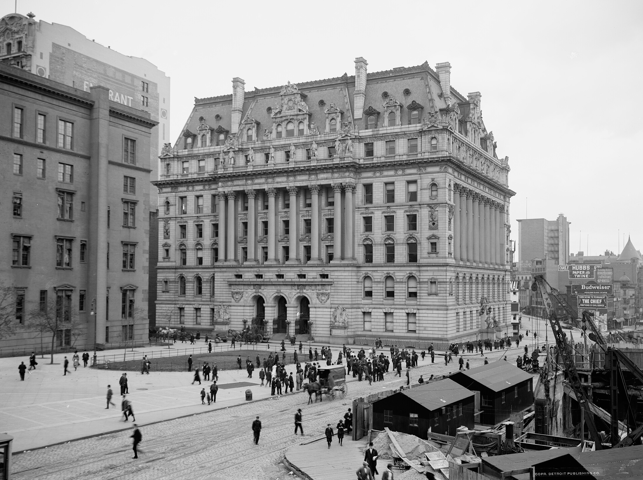 a black and white photo of the building with people walking in front and horse drawn carriages