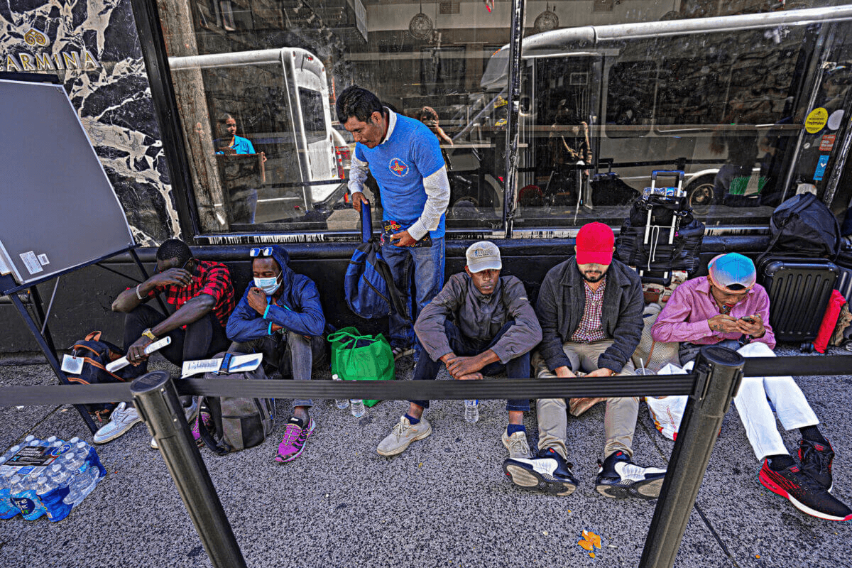 people sitting on the sidewalk outside a migrant center