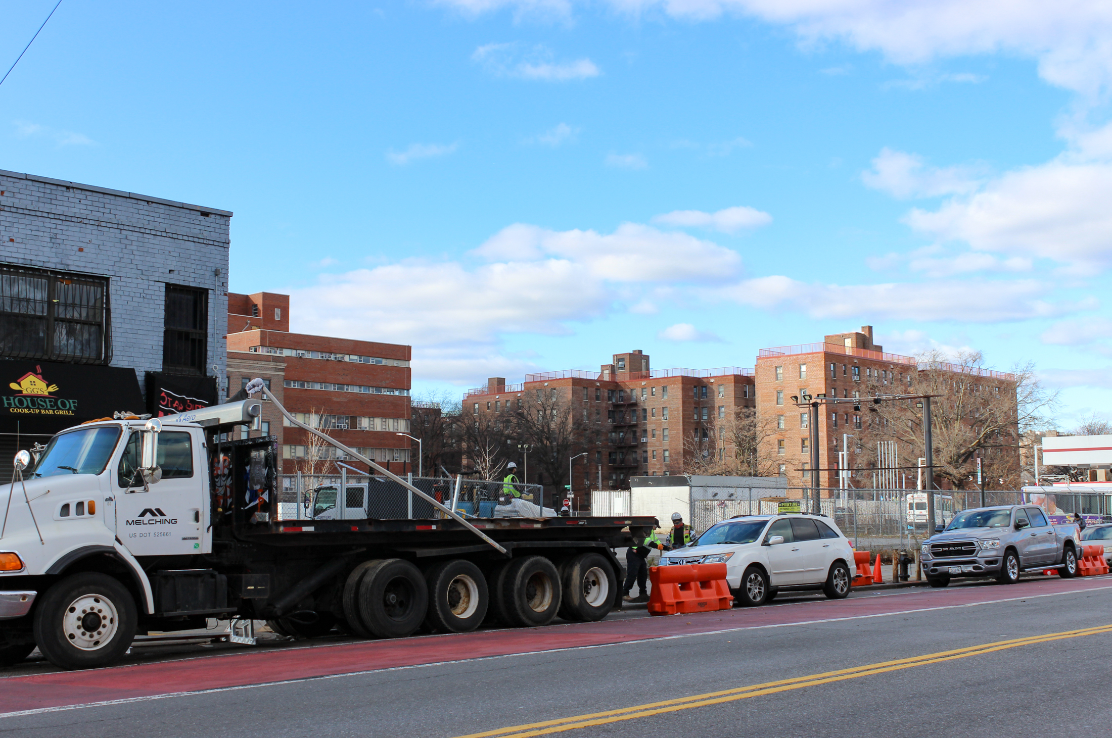 view across street to chain link fence around parking lot with traffic in front