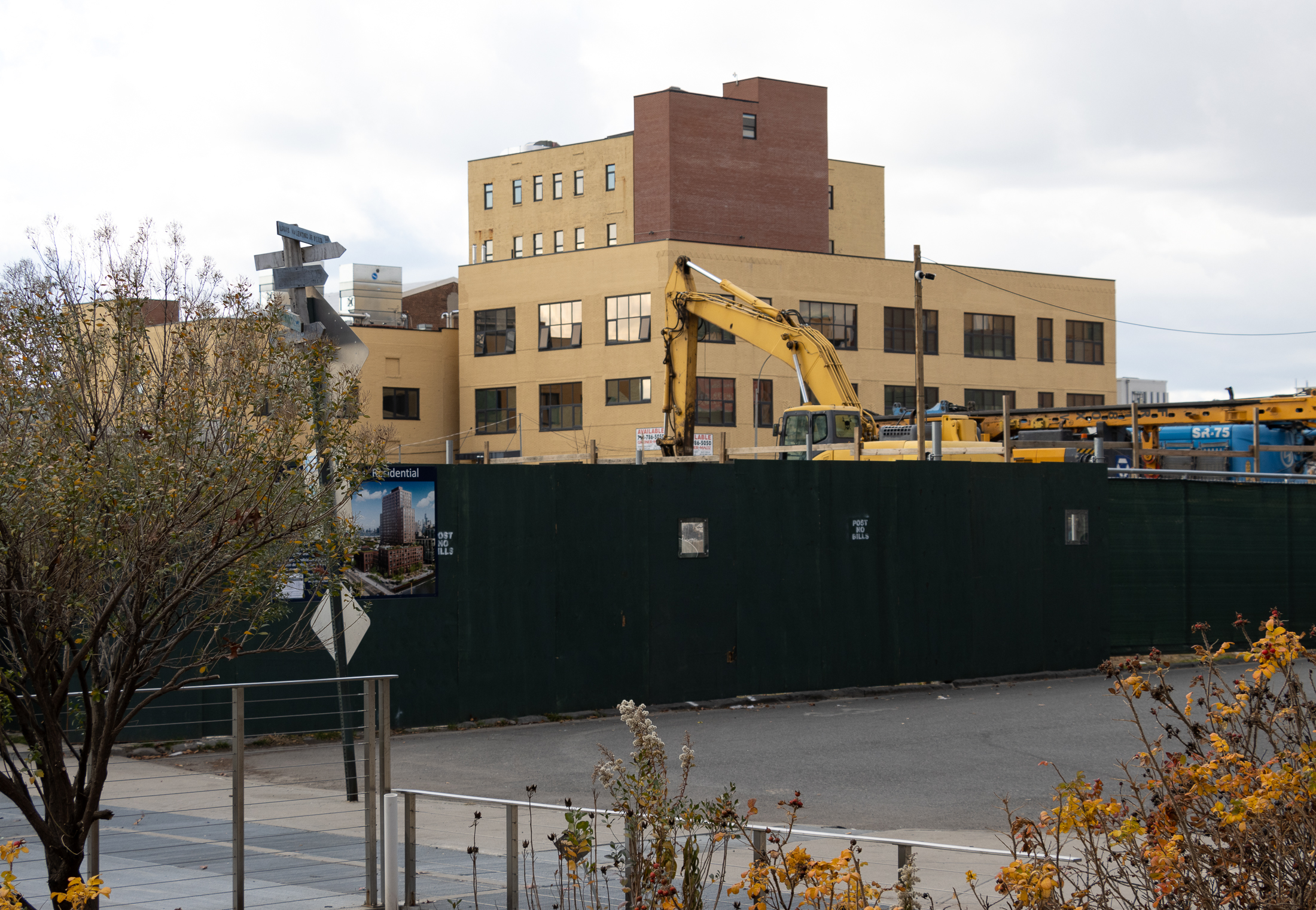construction fence with a rendering and yellow brick buildings behind it