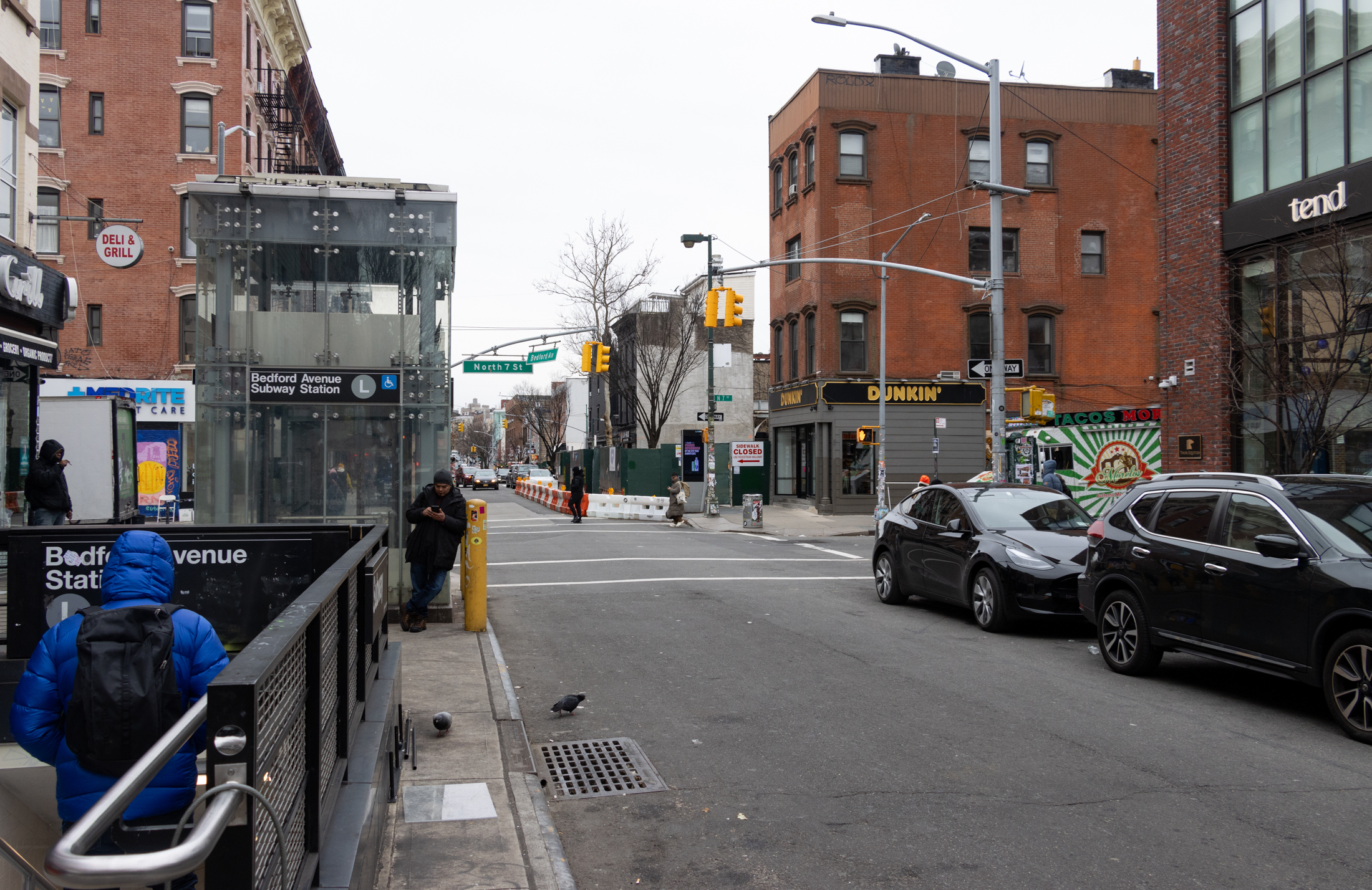 a person goes down the steps of the bedford avenue l station with the project site in the distance