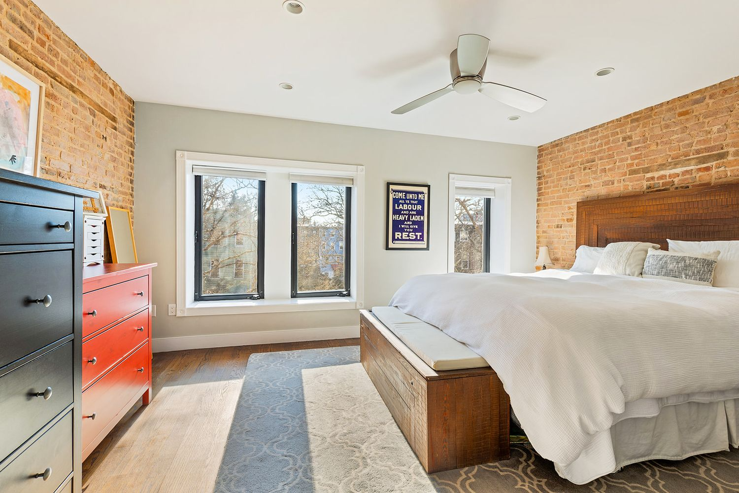 bedroom with dark floor, exposed brick walls and three windows