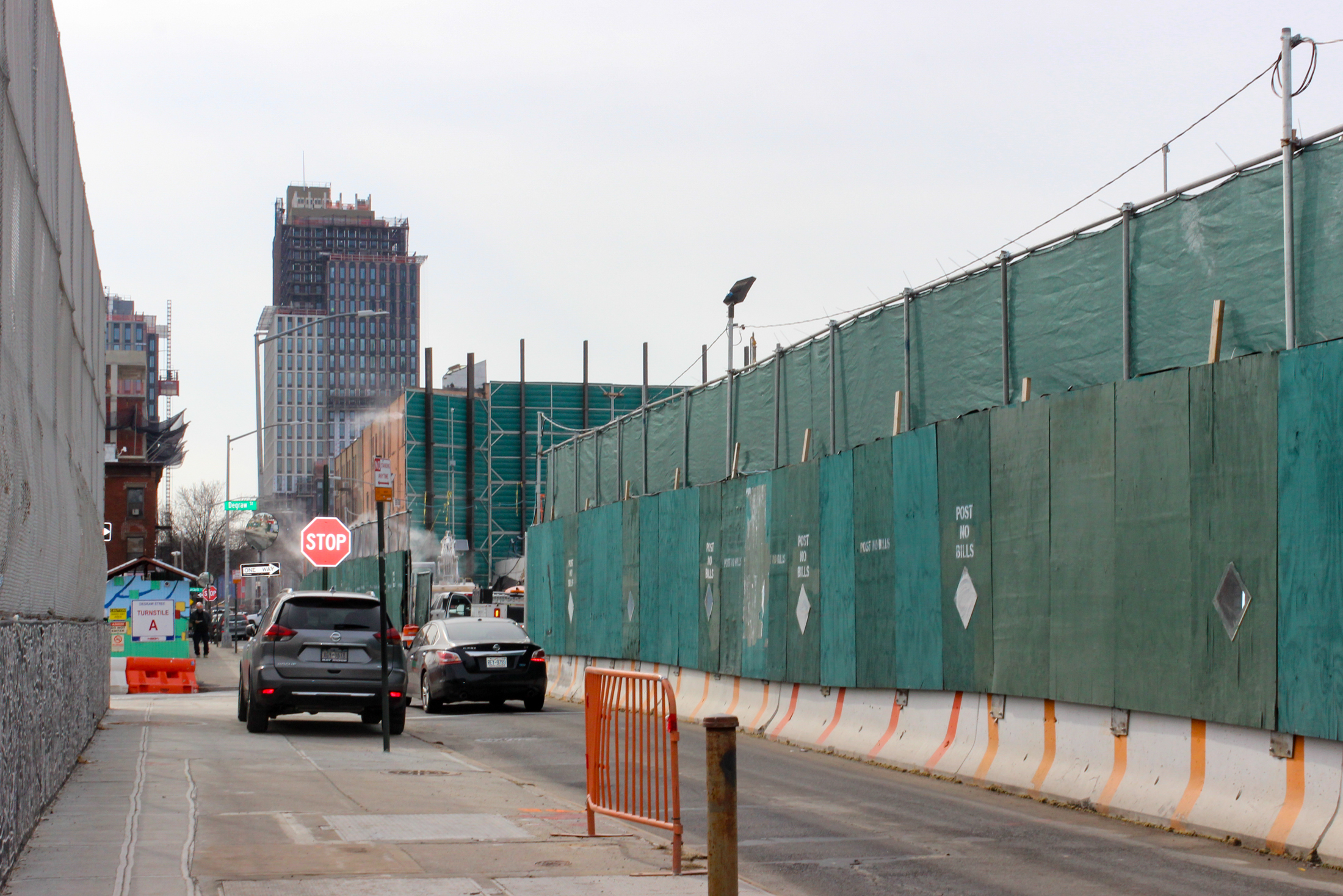 cars driving by green construction fences