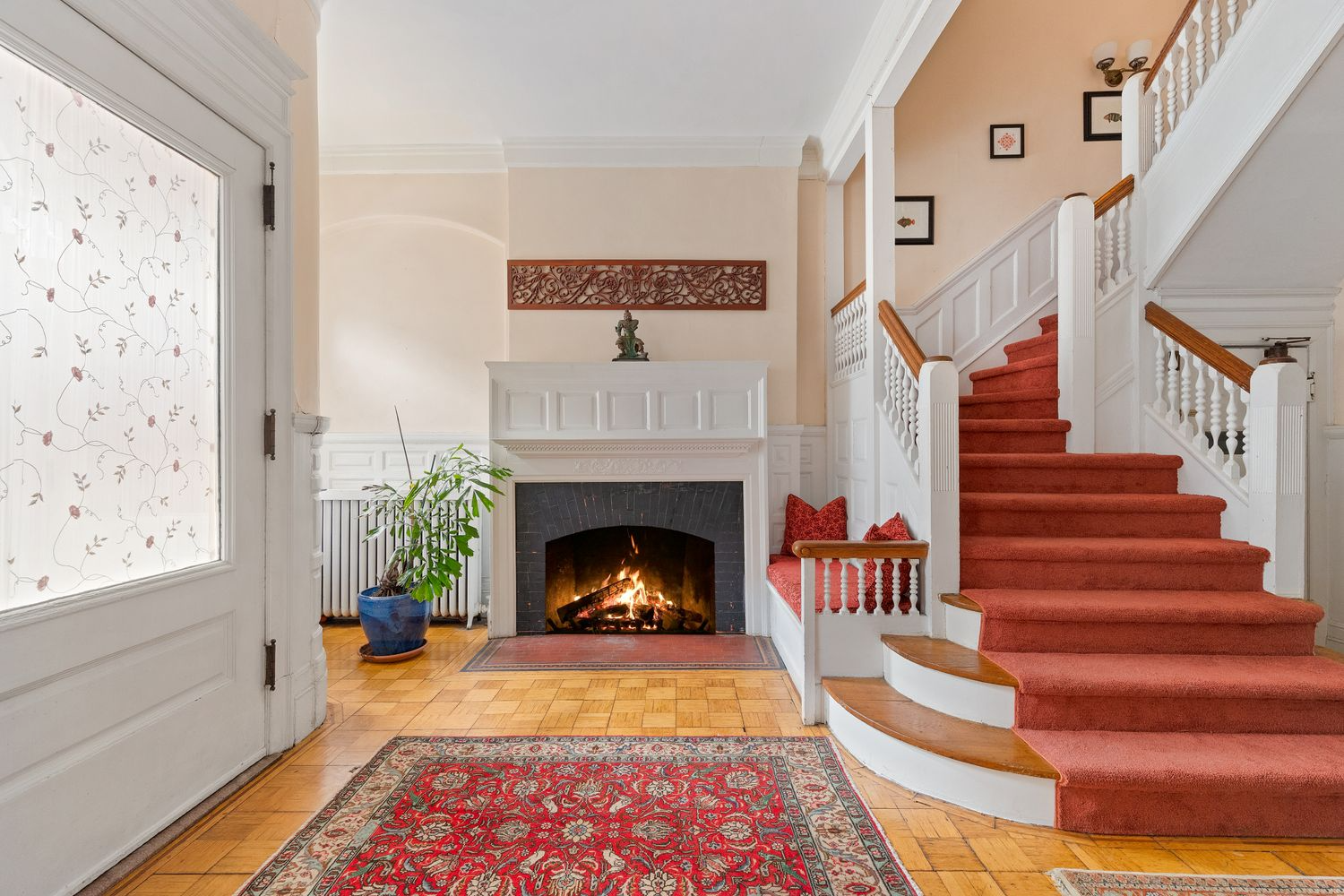 fireplace in the entry hall with wainscoting and a stair with a built-in bench and all woodwork painted white