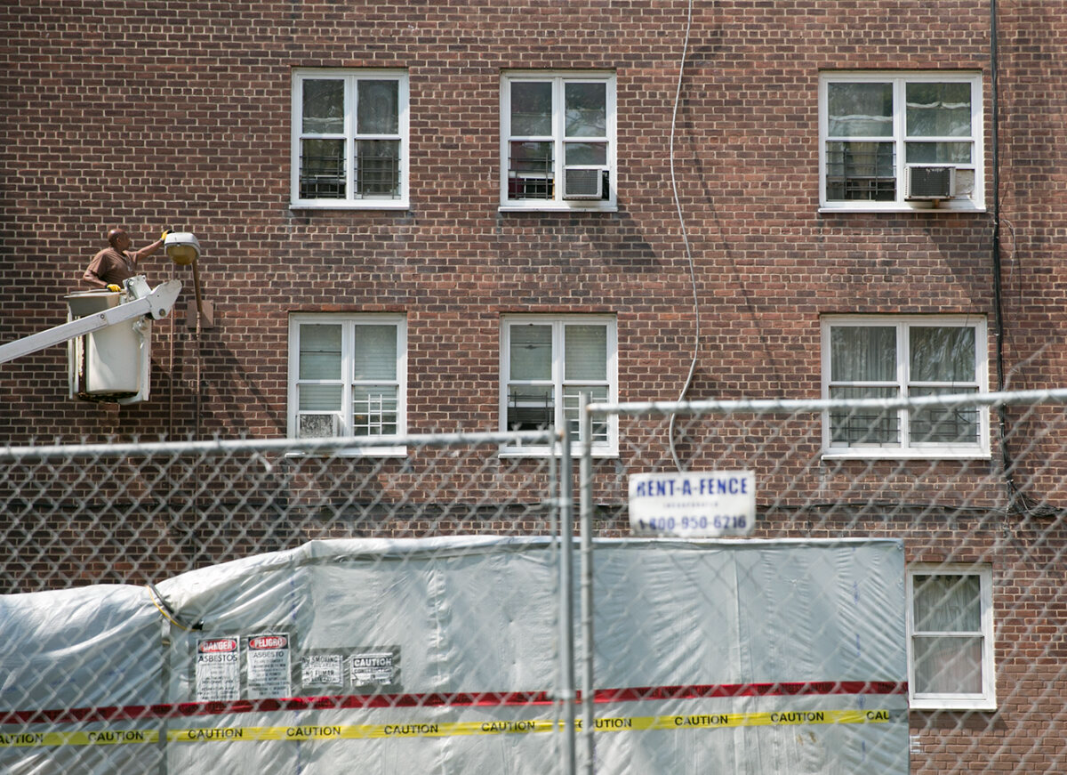 red hook houses - worker in a crane adjusting a light fixture on the exterior of the building