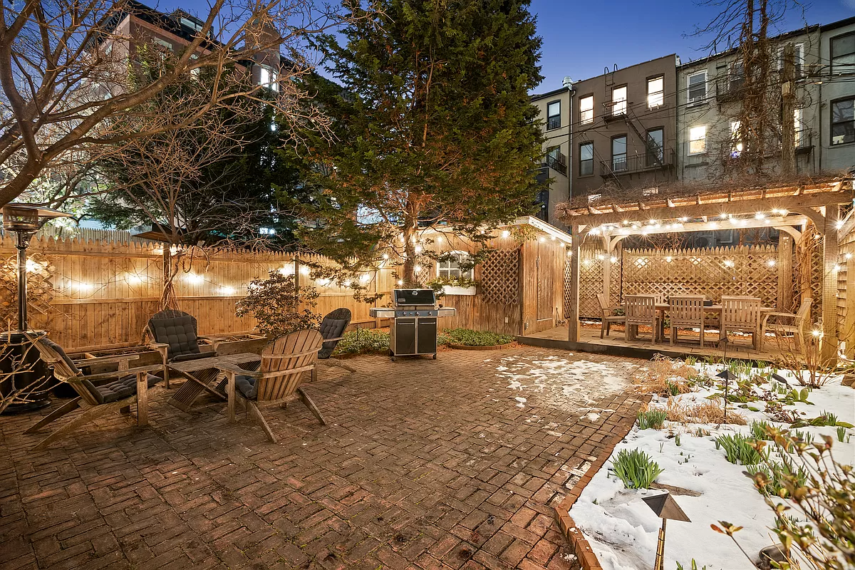 rear yard at night in the snow with brick paved patio, a shed and pergola