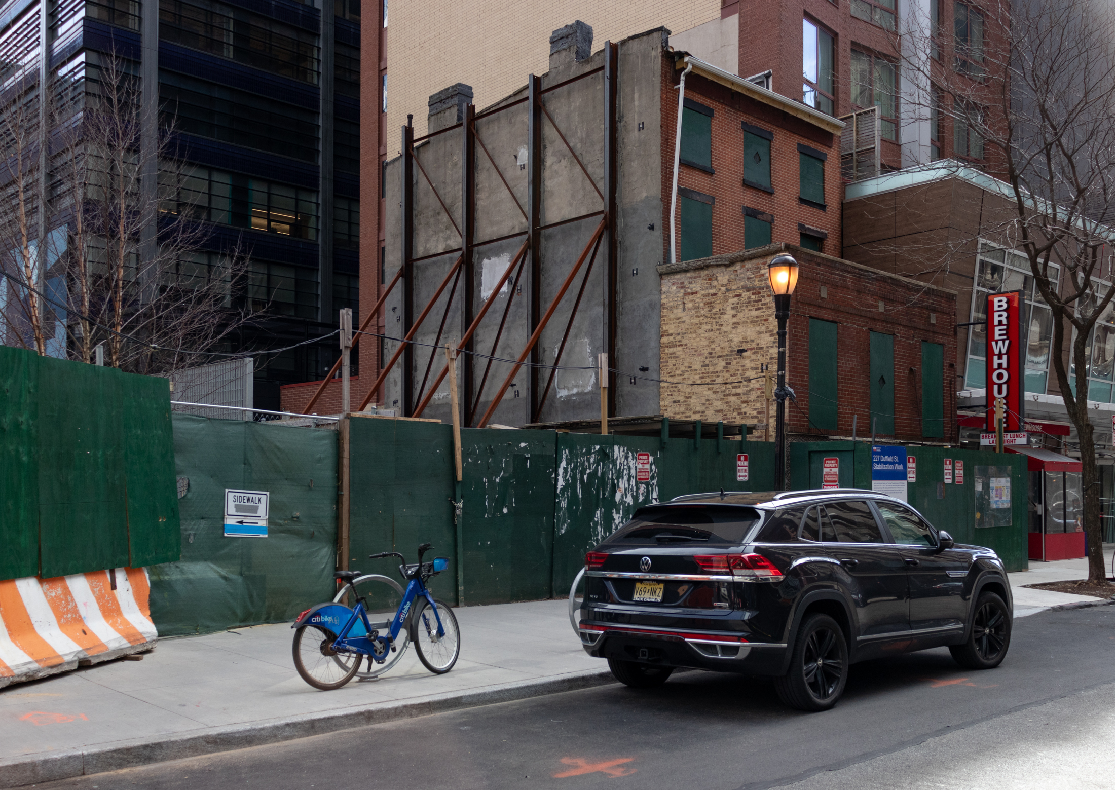 brick house with structural supports and a green construction fence