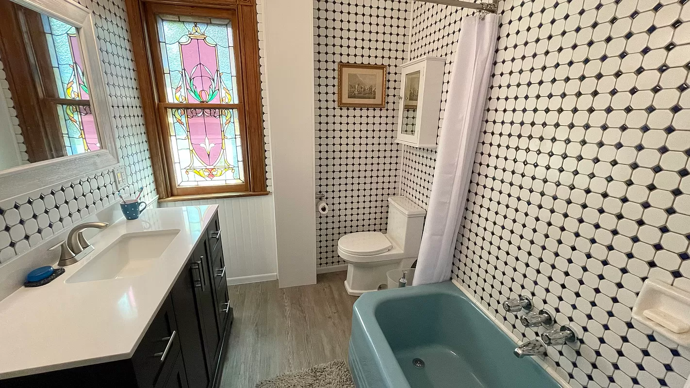 bathroom with black and white wall tile, blue tub and a stained glass window