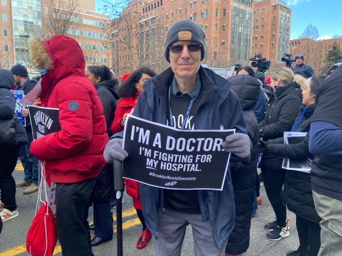 a doctor holds a sign with "i'm a doctor i'm fighting for my hospital"