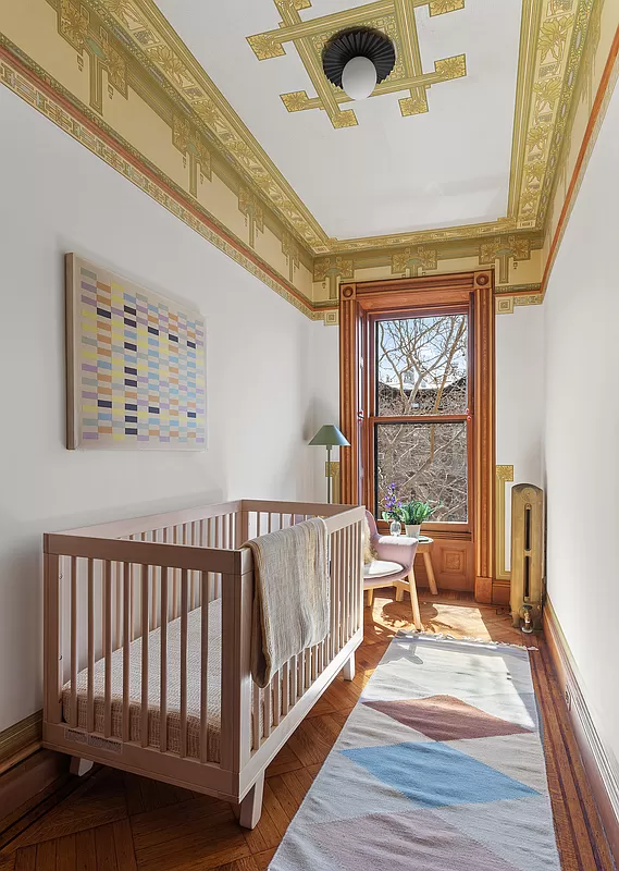 narrow bedroom set up as a nursery with wallpaper border and ceiling details