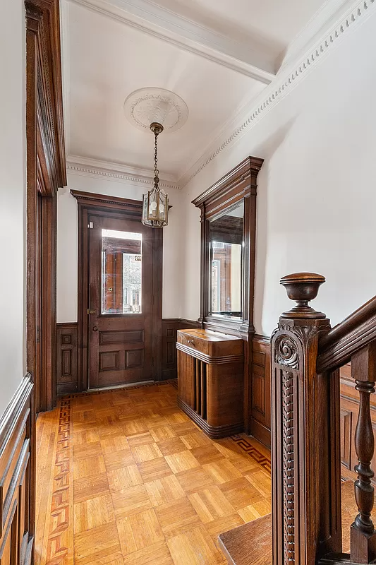 front entry with ornate newel post on stair, wainscoting and a wood floor
