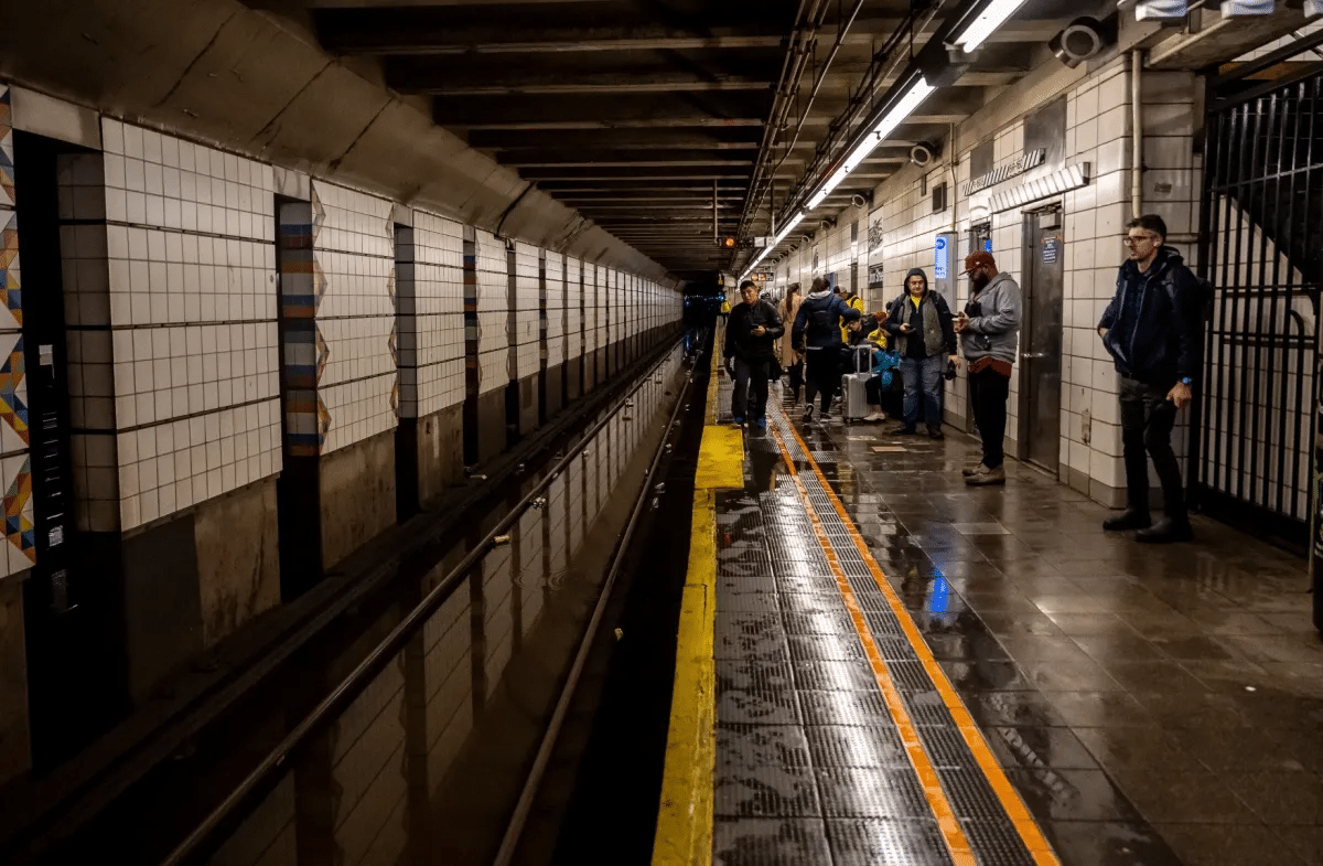 people wait on a wet subway platform