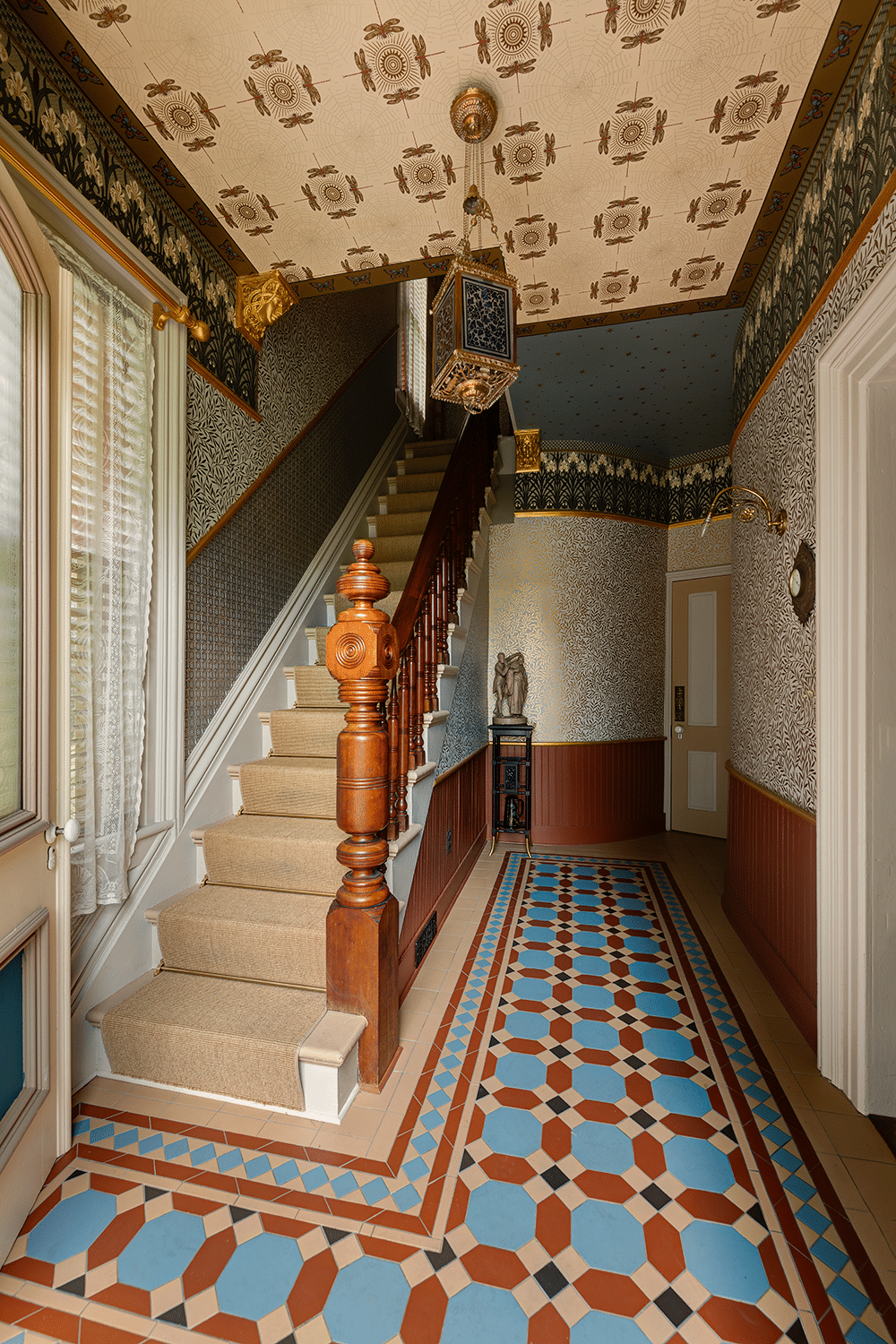 entry with original stair and newel post, encaustic tile sand wall and ceiling papers