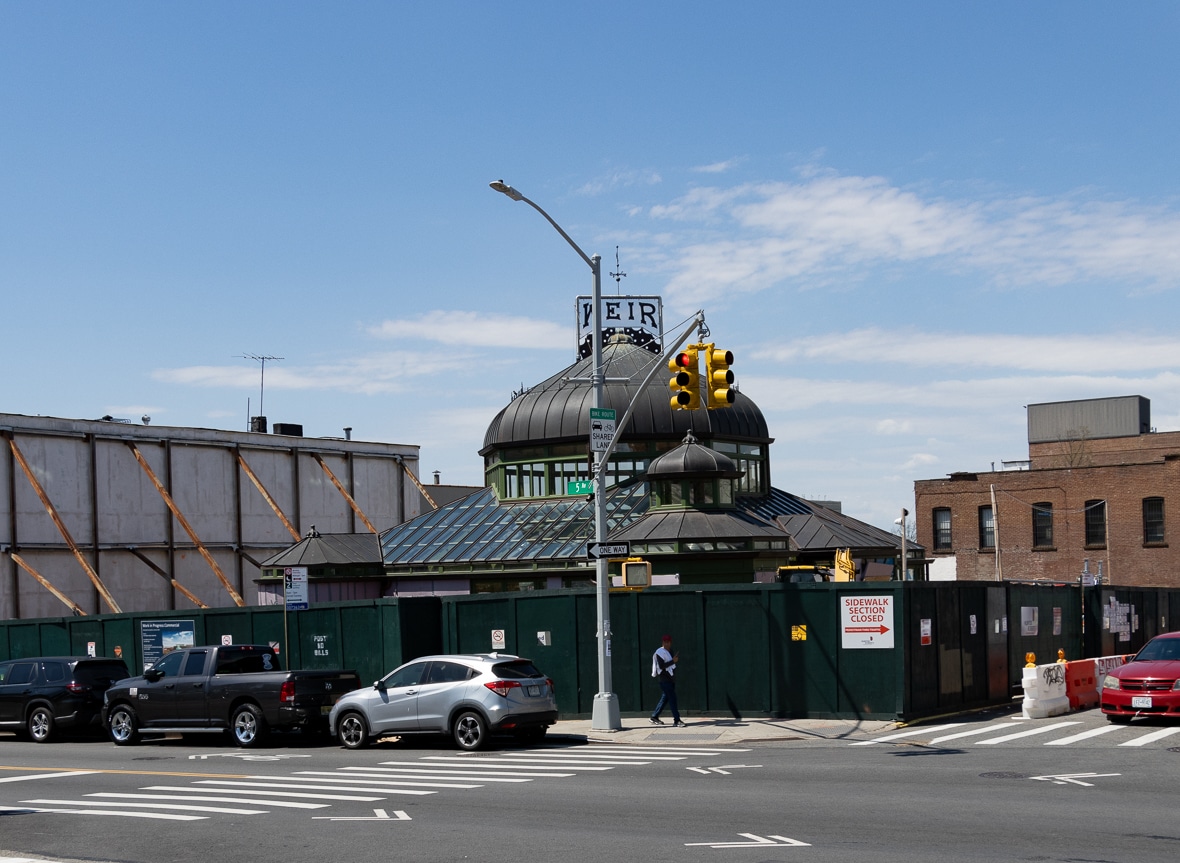 the historic greenhouse at the corner of 25th street and 5th avenue with a construction fence surrounding it