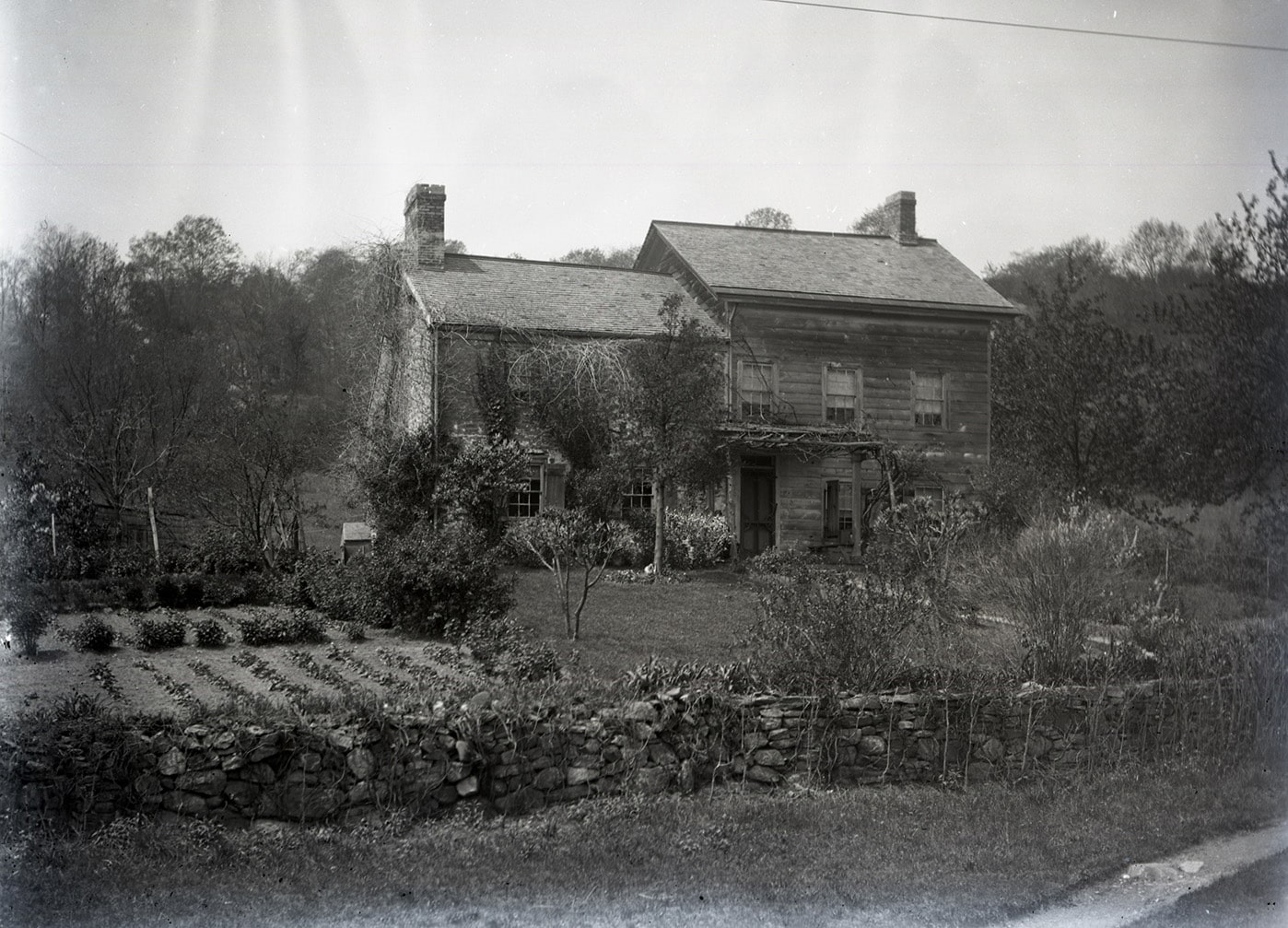 black and white photo showing a stone dwelling with a frame addition