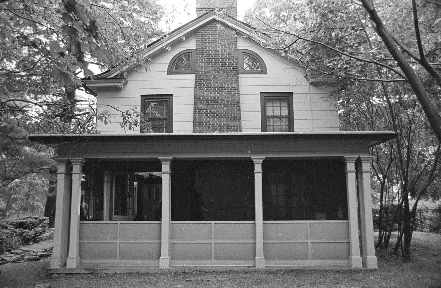 black and white photo showing a gabled end with lunette windows and a columned porch