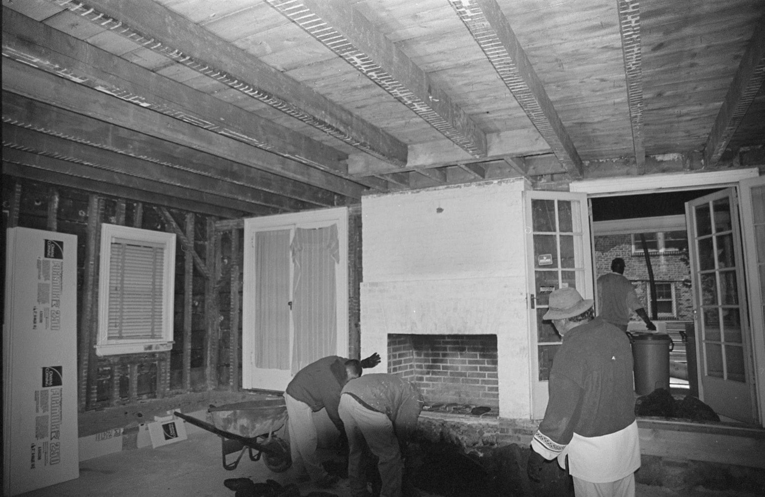 black and white photo of people working in a room with exposed room beams and no plaster on walls