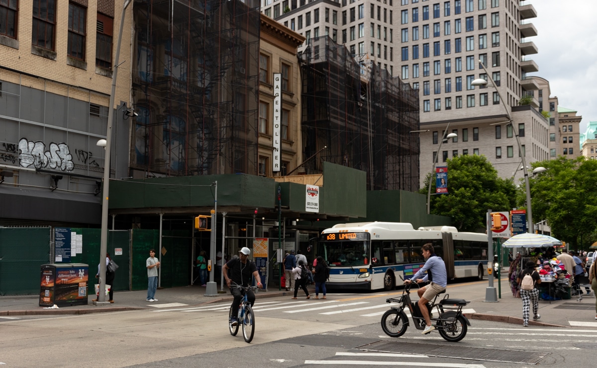 brooklyn - fulton street with bikers passing buildings under scaffolding