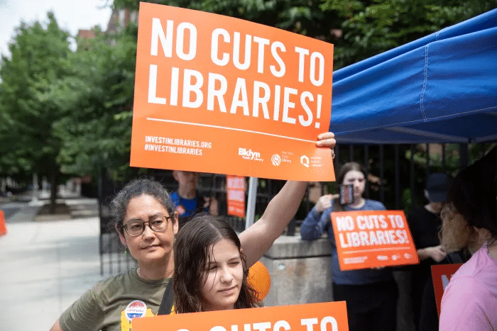 people holding signs with "no cuts to libraries"