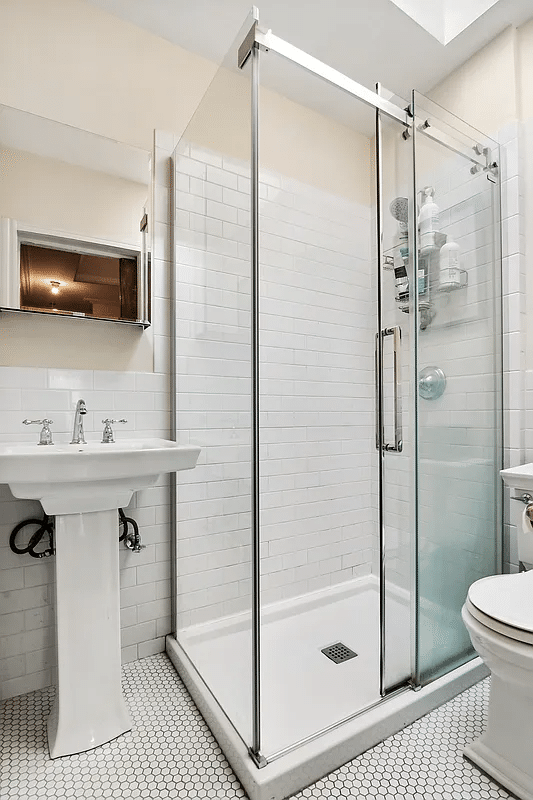 bathroom with glass doors to shower, white fixtures and wall tile