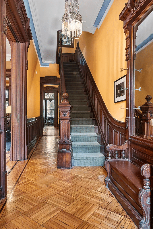 entry hall with wood floor, wainscoting, stair and a mirror with bench