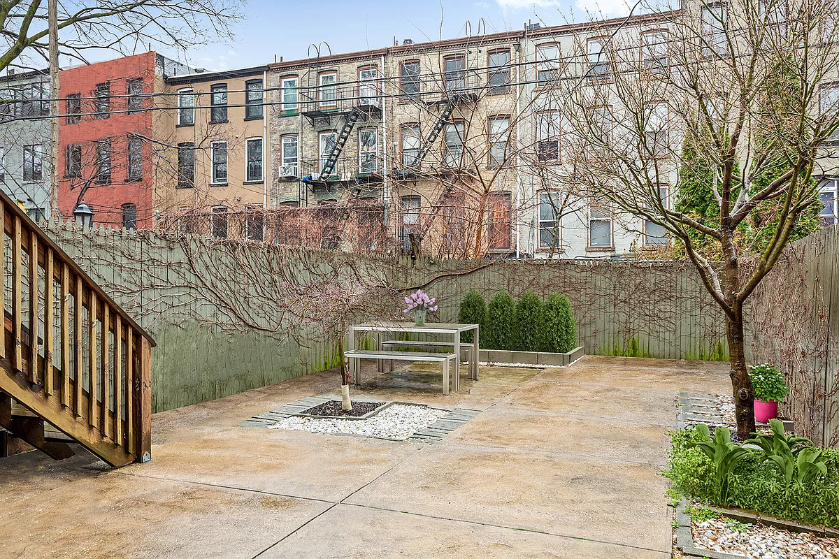 paved rear yard with a few planting beds