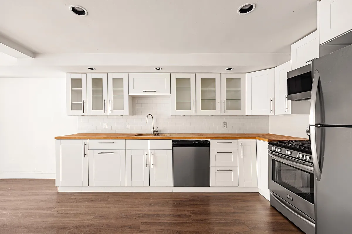 renovated kitchen on the garden level with white cabinets, stainless steel appliances