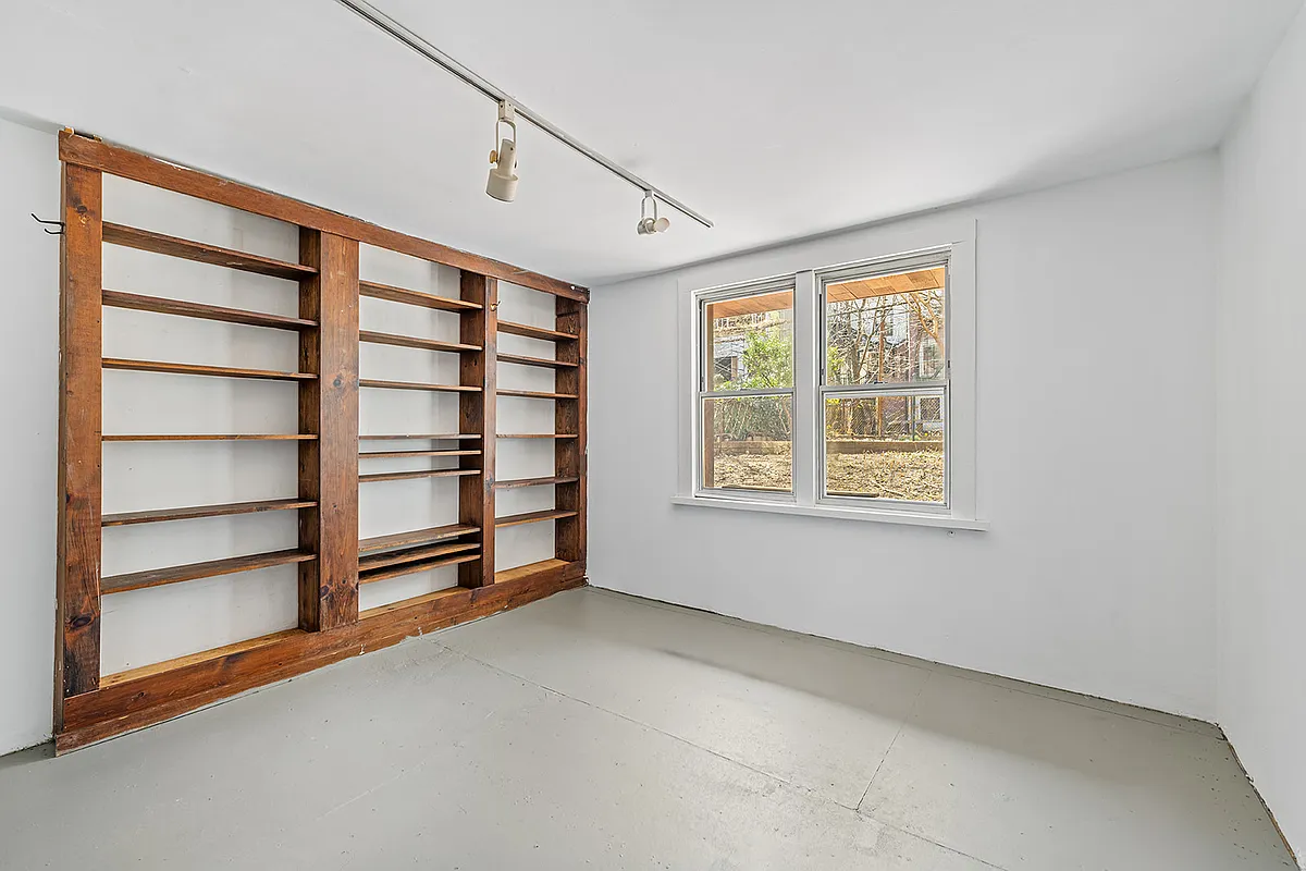 garden level room with plywood floor, bookshelves, and windows to rear yard