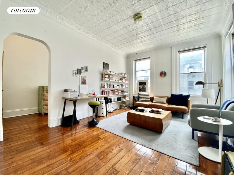 living room with wood floor, tin ceiling, arched doorway to bedroom