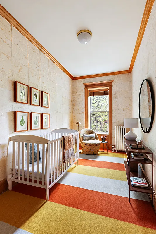 narrow bedroom set up as a nursery with bright striped rug in orange and yellow