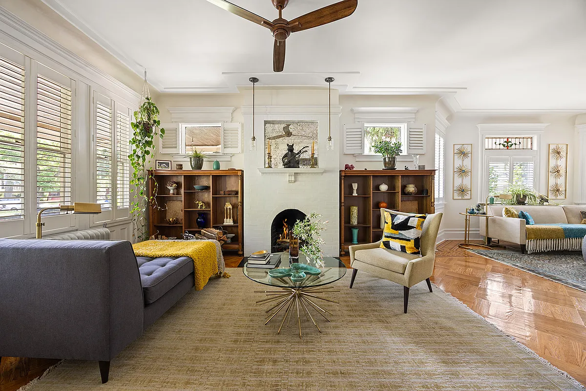 living room with wood floor, windows looking out to porch, fireplace, and a ceiling fan
